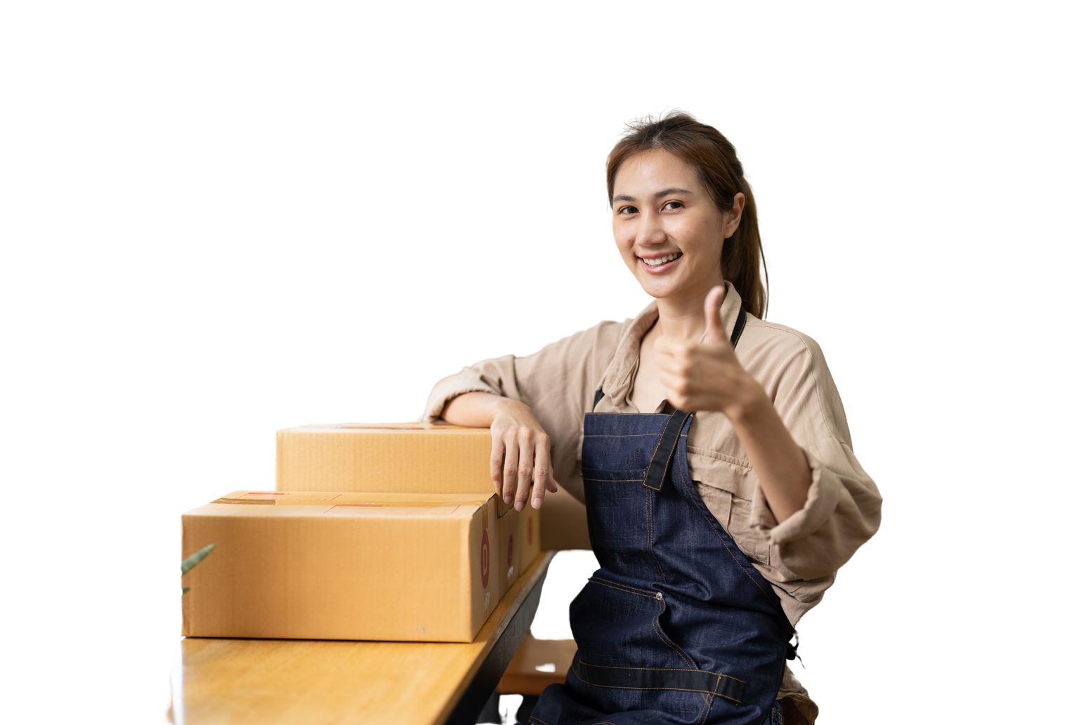 a business owner in overalls sitting at a table with boxes doing the thumbs up